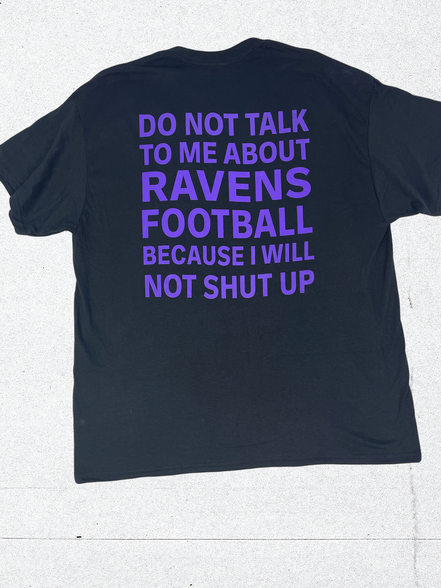 A T-shirt that is Black in color, showing the back of the t-shirt with purple text that says "DO NOT TALK TO ME ABOUT RAVENS FOOTBALL BECAUSE I WILL NOT SHUT UP"