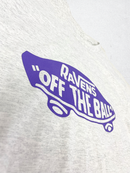 A closeup of an ash white t shirt with a purple design in the middle that looks like a skateboard and says Ra VENs Off the ball. 